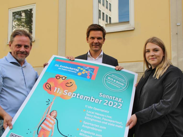 Zwei Männer und eine Frau präsentieren ein Plakat zum Entdeckertag 2022.