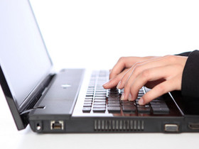Zu sehen sind ein Laptop und zwei Hände, die auf der Tastatur schreiben