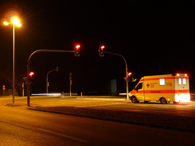 Ein Rettungswagen hält an einer Ampel, die Bremslichter und die Lichtzeichen der Ampel leuchten rot.