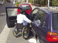 Rollstuhlfahrerin neben offener Autotür