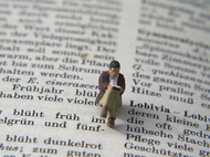 Ein kleines Figürchen sitzt auf einem aufgeschlagenen Buch und liest.