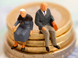 Kleine Puppen eines alten Mannes und einer alten Frau sitzen auf dem Rand von Geldmünzen.