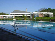 Das mit Wasser gefüllte Aussenbecken des Hallenfreibades Burgdorf ohne Badegäste bei strahlend blauem Himmel, im Hintergrund die Gebäude des Hallenbades, die sich im Wasser spiegeln