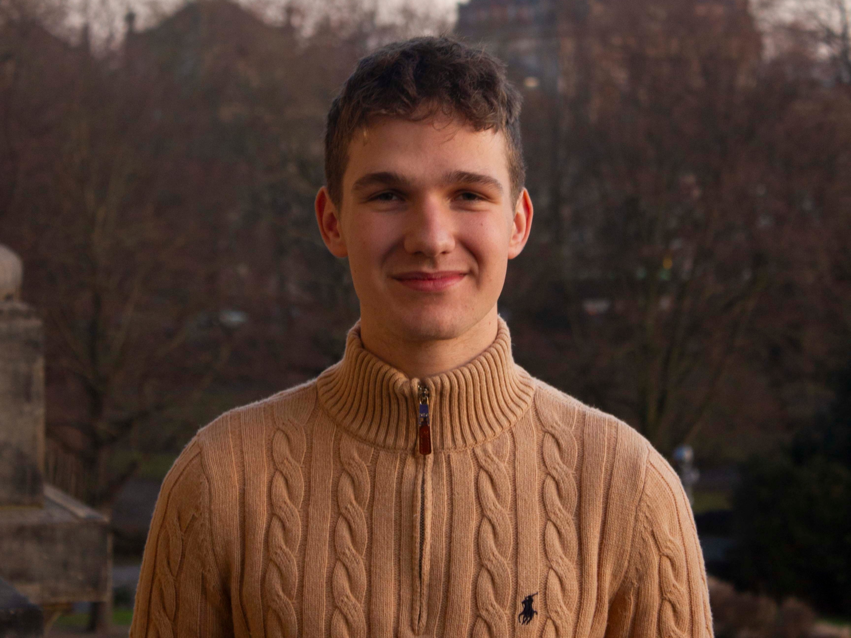 Ein junger Mann schaut in die Kamera und l&auml;chelt.