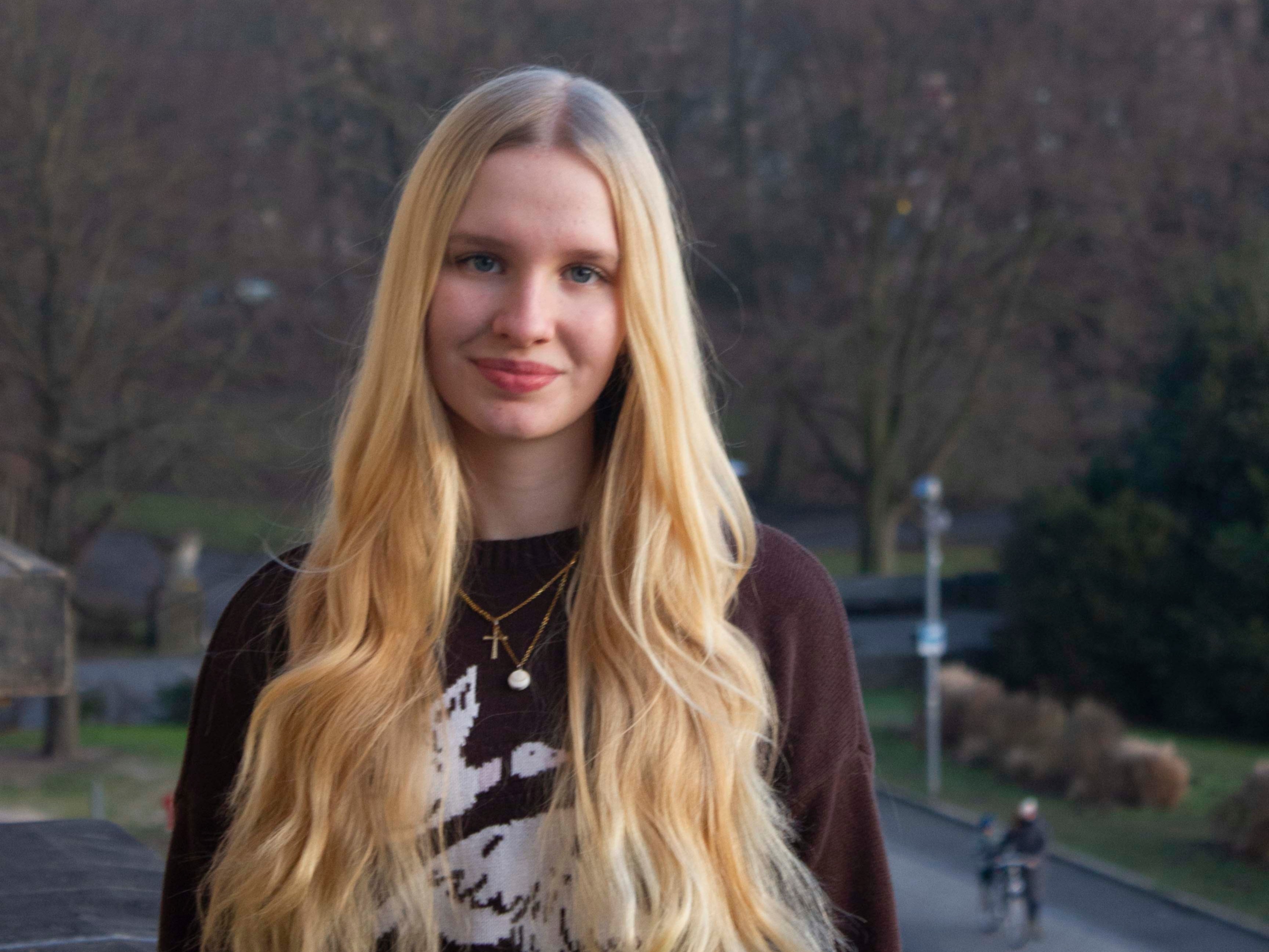 Eine junge Frau schaut in die Kamera und l&auml;chelt.