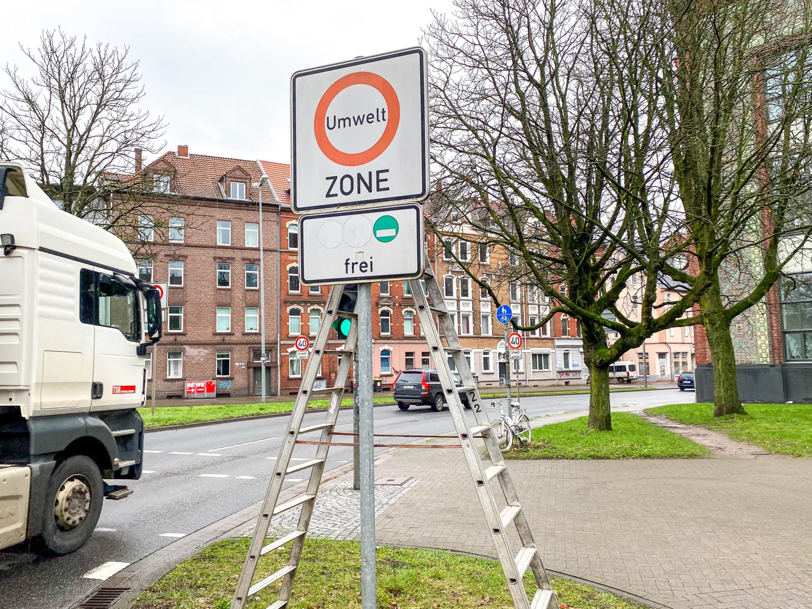 Ein Schild. Dahinter steht eine Leiter, auf der zwei Männer stehen, die das Schild abmontieren.