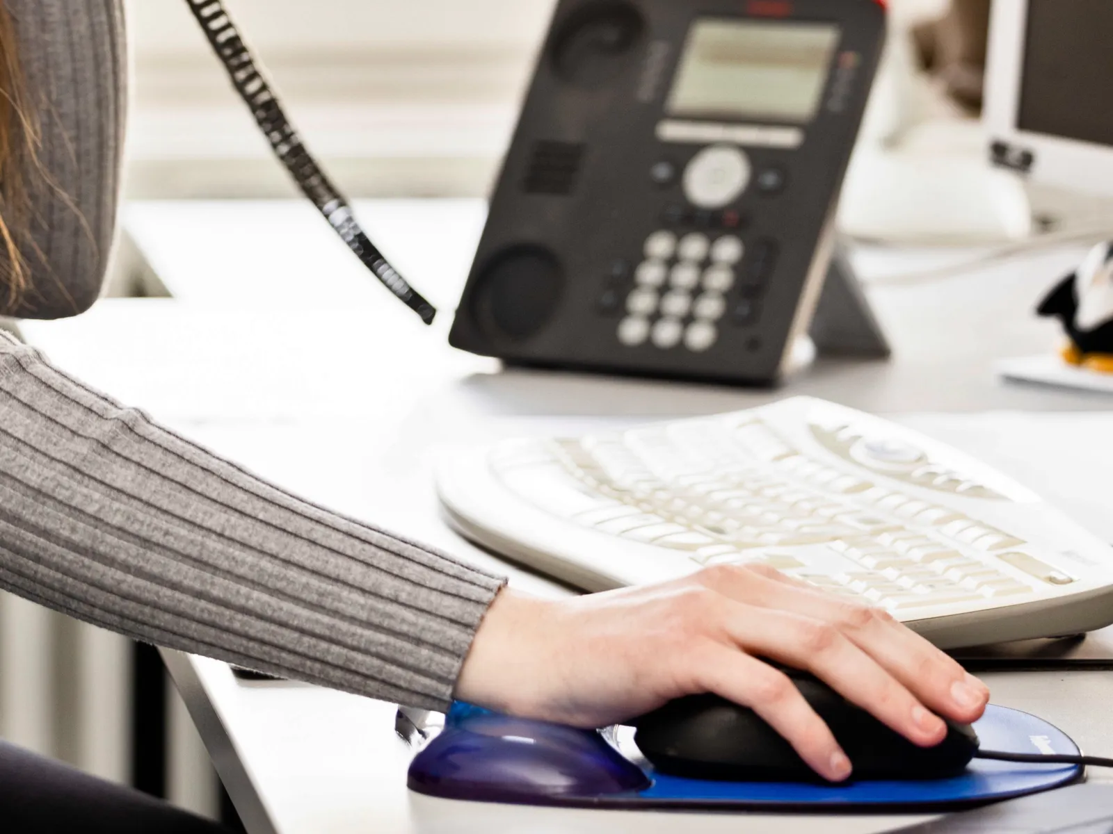 Etwas fragen und Antworten bekommen: Eine Hand bewegt eine Computermaus, vom Telefon ist der Hörer abgenommen und die Person telefoniert mit der anderen Hand.