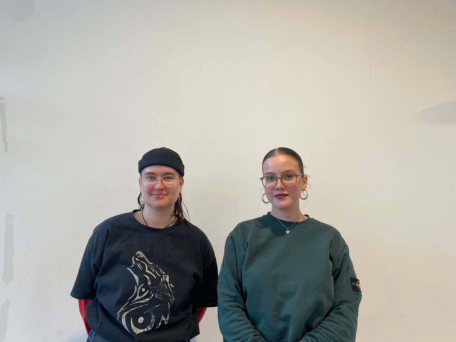 Zwei junge Menschen stehen lächelnd vor einer weißen Wand.