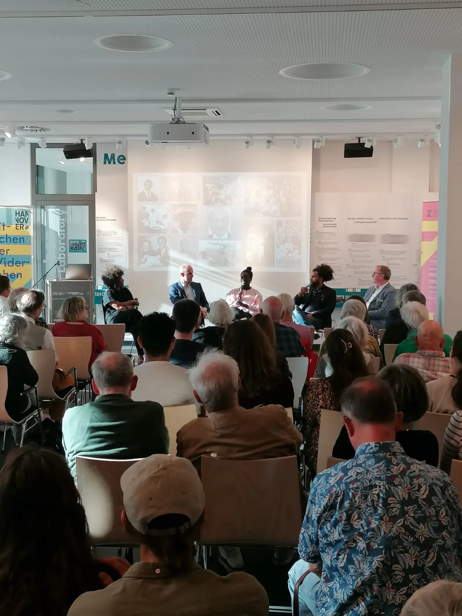Eine Veranstaltung im ZeitZentrum Zivilcourage. Bild von hinten aus dem Publikum. Zu sehen sind gef&uuml;llte Reihen von Hinterk&ouml;pfen, sie sind alle auf das Podiumsgespr&auml;ch gerichtet. Im Podium sitzen f&uuml;nf Personen, darunter Brenda Davina, Dr. Jens Binner und Oberb&uuml;rgermeister Belilt Onay. Brenda Davina spricht in das Mikrofon.