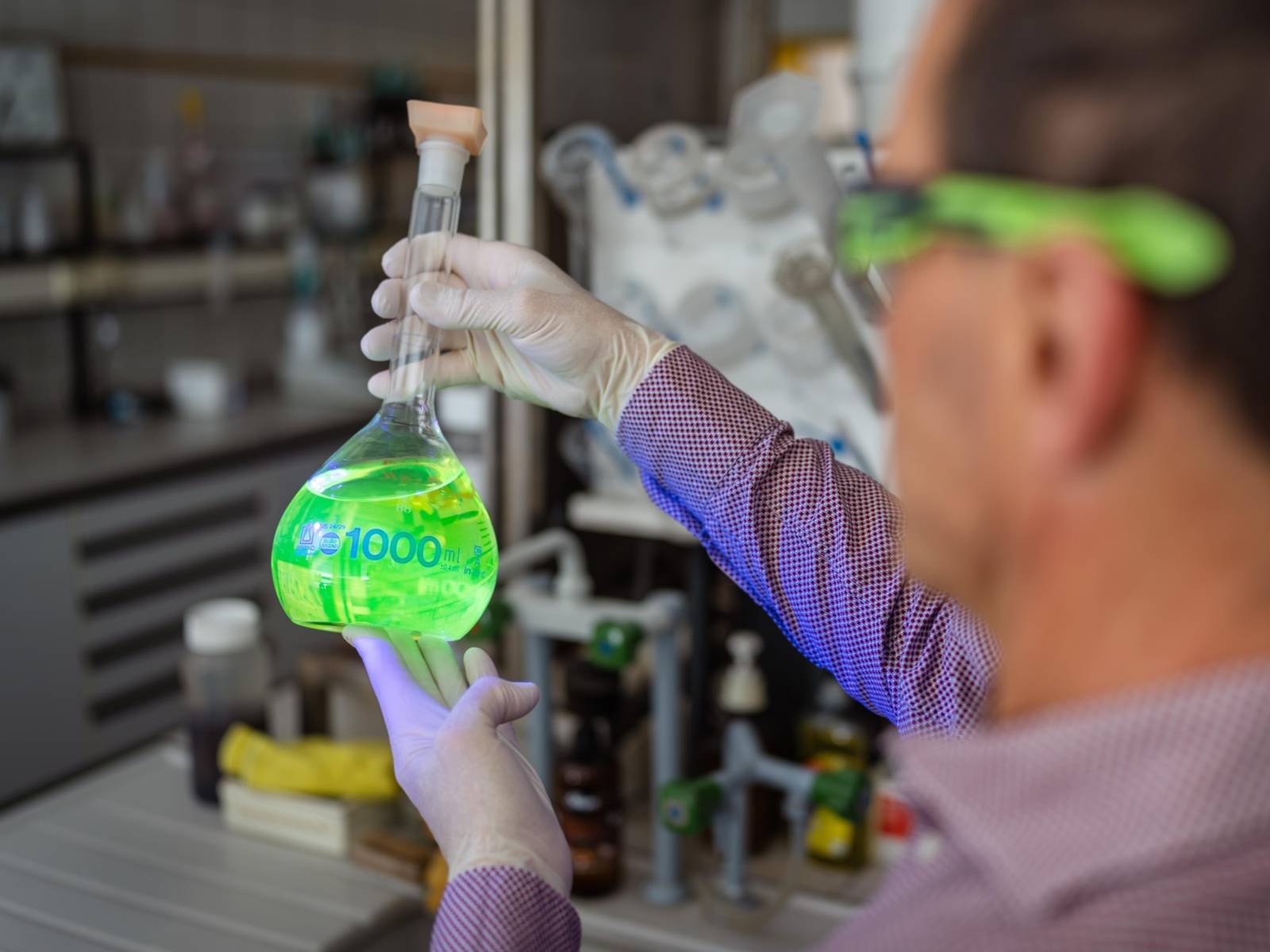Ein Mann im Labor hält einen Kolben mit grüner Flüssigkeit in der Hand