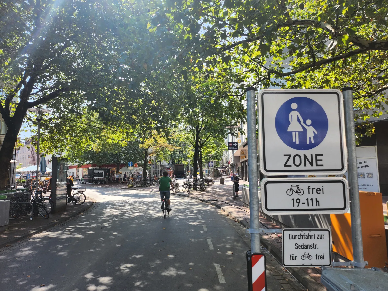 Eine Straße mit Radfahrer und Bäumen, rechts ein Schild Fußgängerzone