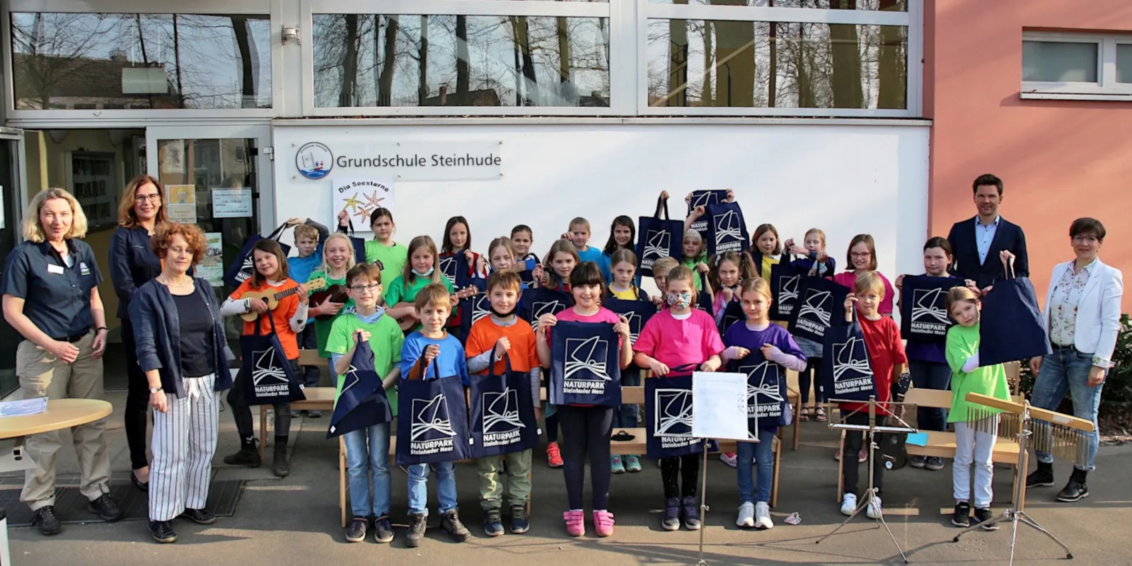 Ein Mann und vier Frauen haben sich gemeinsam mit 29 Kindern zu einem Gruppenbild aufgestellt. Einige Instrumente sind im Bild, die Kinder halten Stoffbeutel mit dem Naturparklogo in den H&auml;nden.