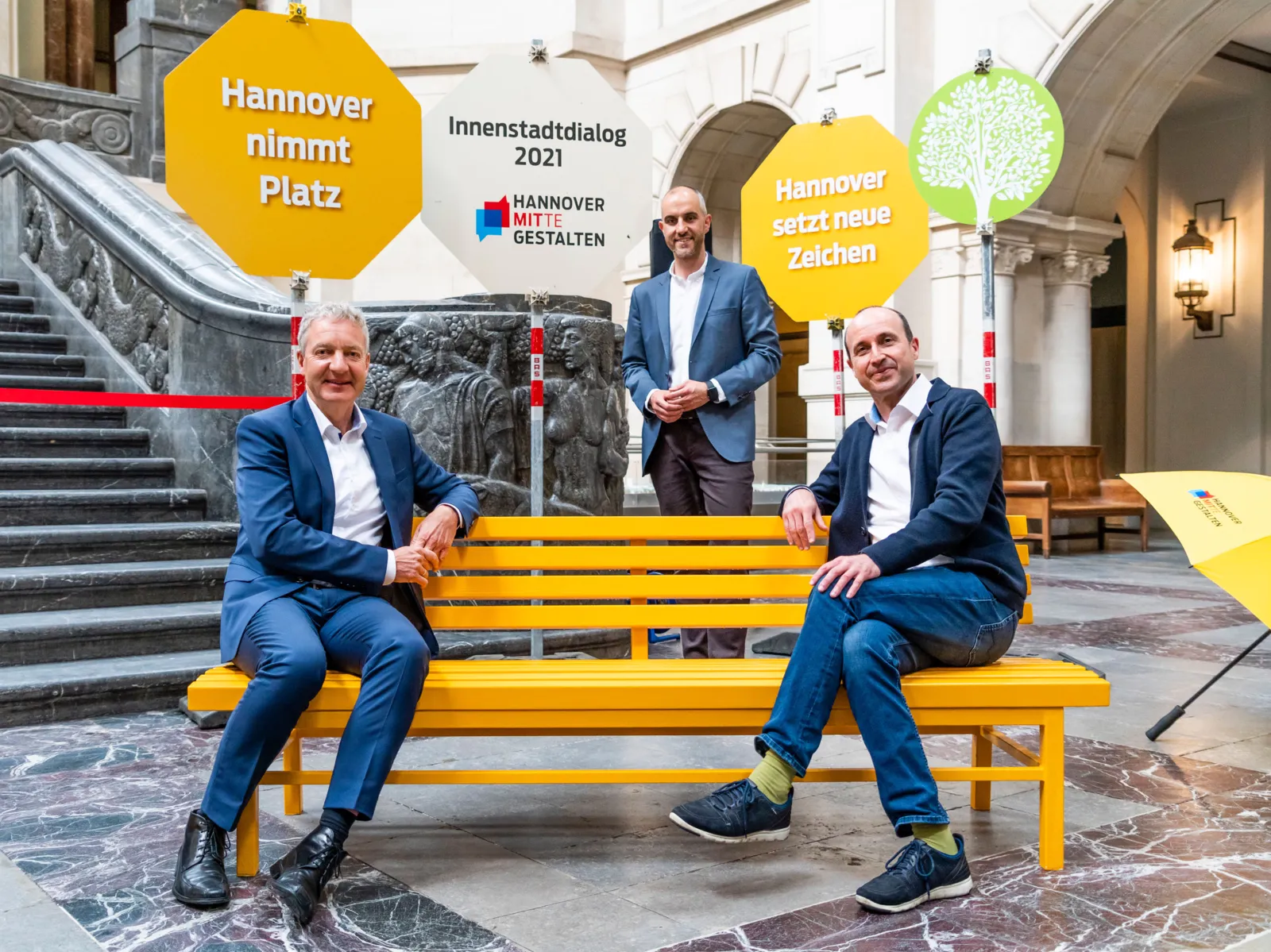 Drei Männer in einer Halle. Drumherum bunte Schilder.