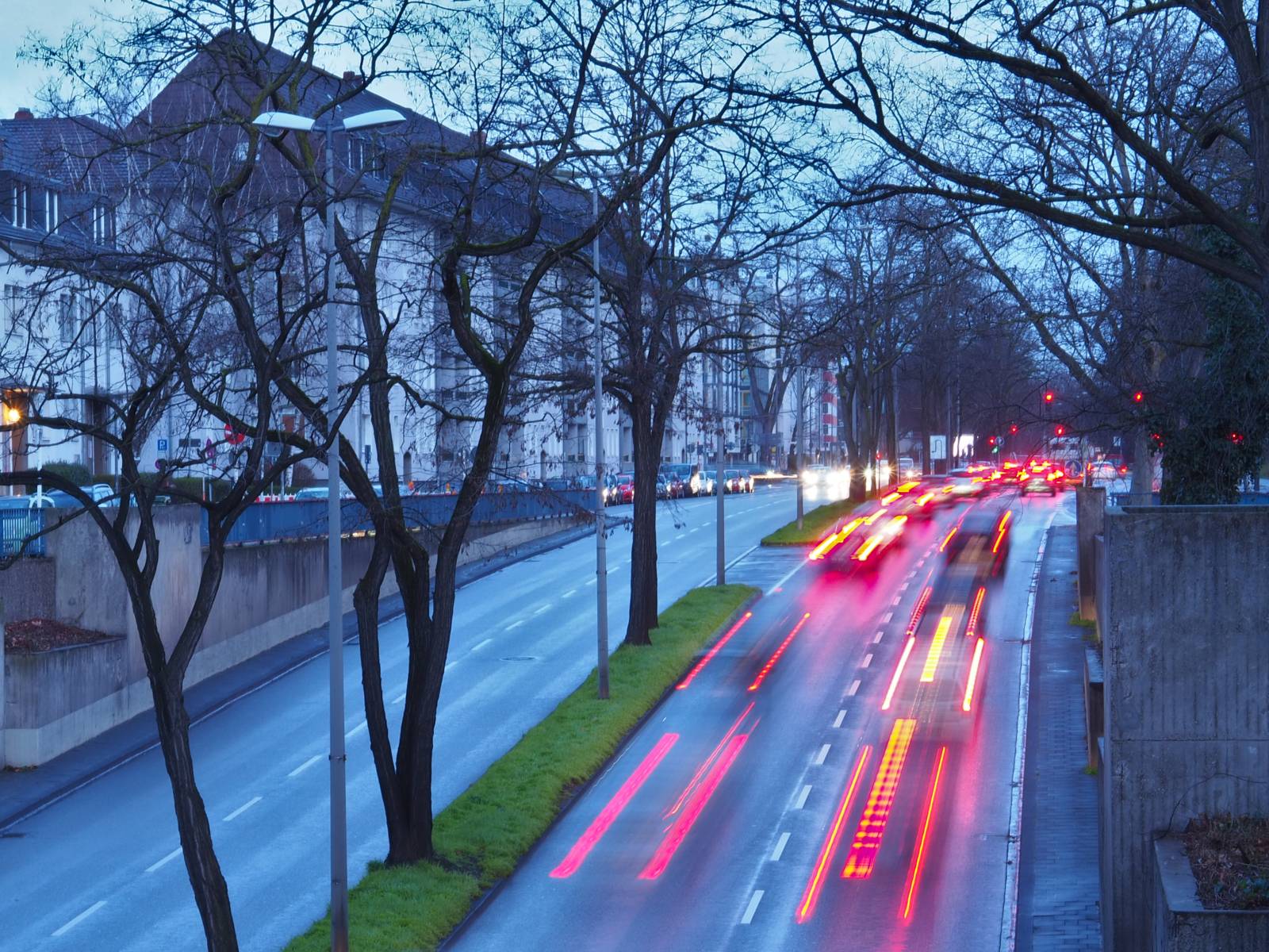 Fahrzeuge fahren auf eine Kreuzung zu, die Lichtzeichen zeigen rot. Lichtspuren zeigen in der Langzeitbelichtung die Bewegung der Fahrzeuge. Weitere Fahrzeuge parken am Straßenrand – rechtmäßig?