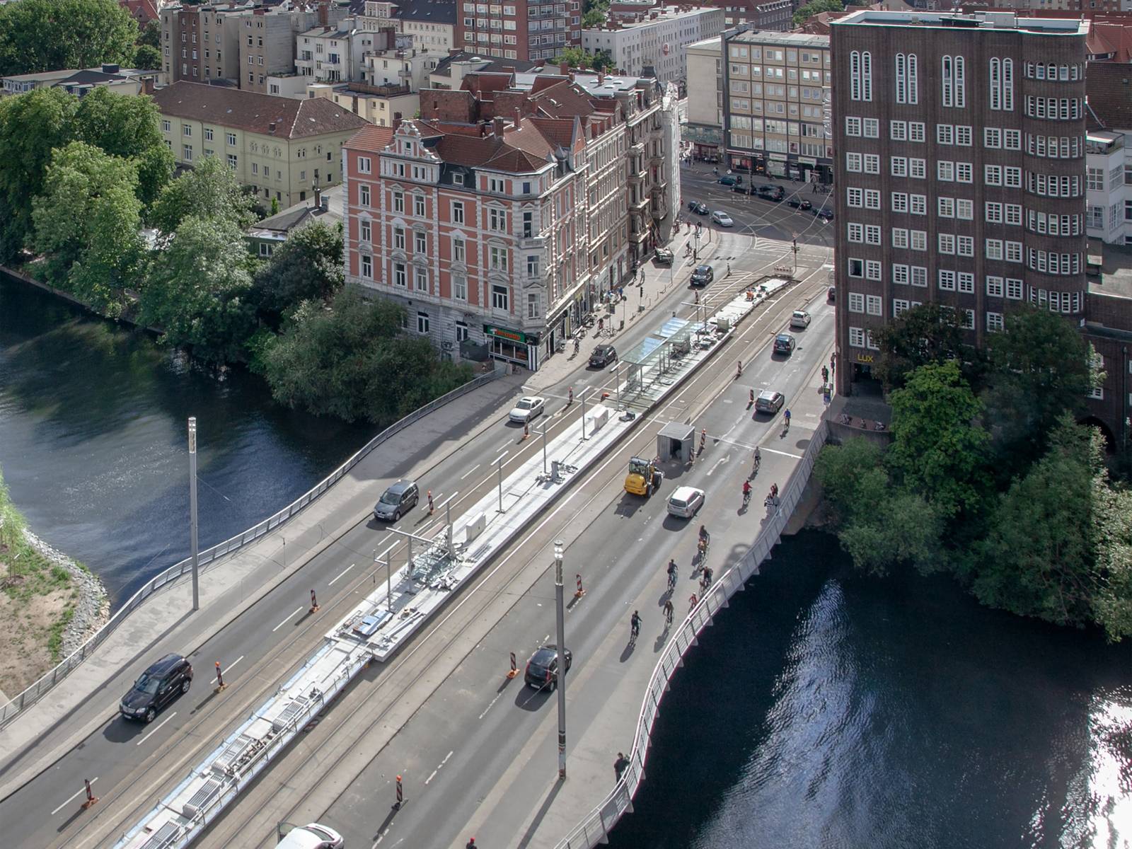 Bild von oben auf eine Brücke mit Straße und Autos, darunter ein Fluss, im Hintergrund Gebäude.