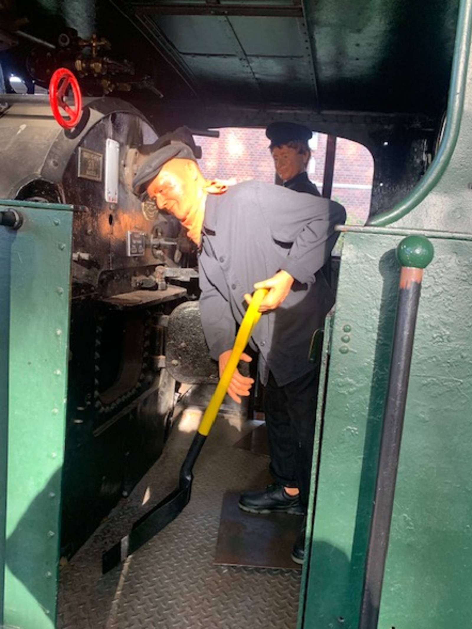 Blick auf den Führerstand einer historischen Eisenbahn, eine Person schaufelt Kohlen.