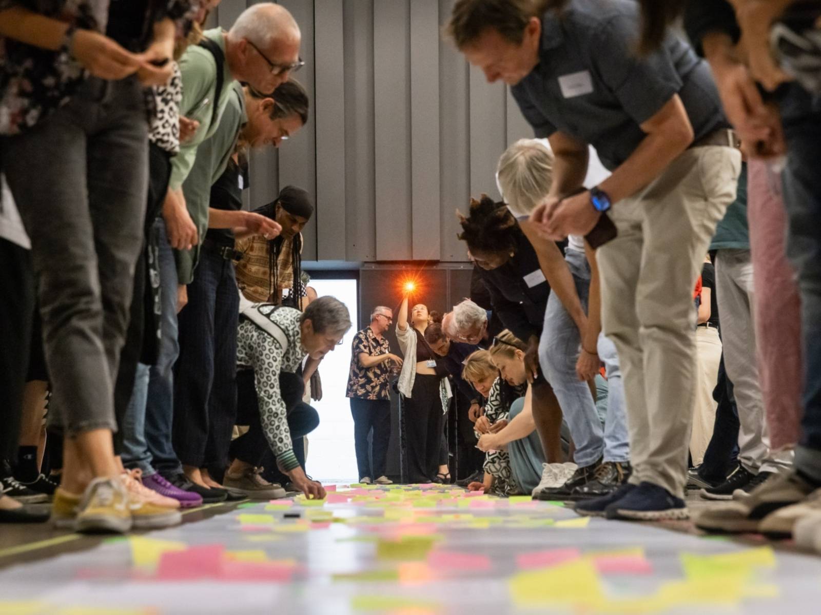 Viele Menschen beugen sich über bunte Klebezettel auf dem Boden.