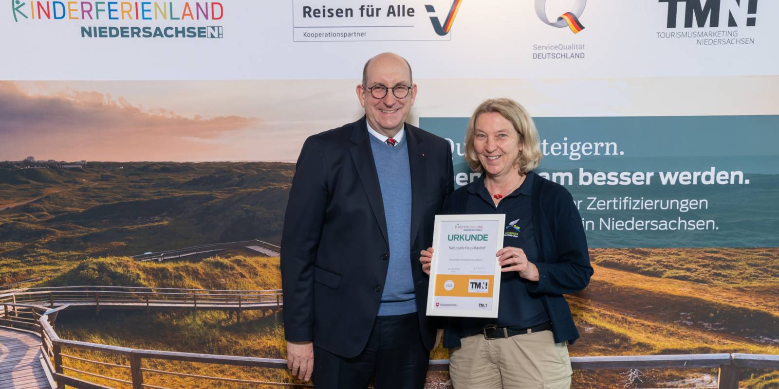 Zwei Personen stehen nebeneinander, eine h&auml;lt eine Urkunde in den H&auml;nden.