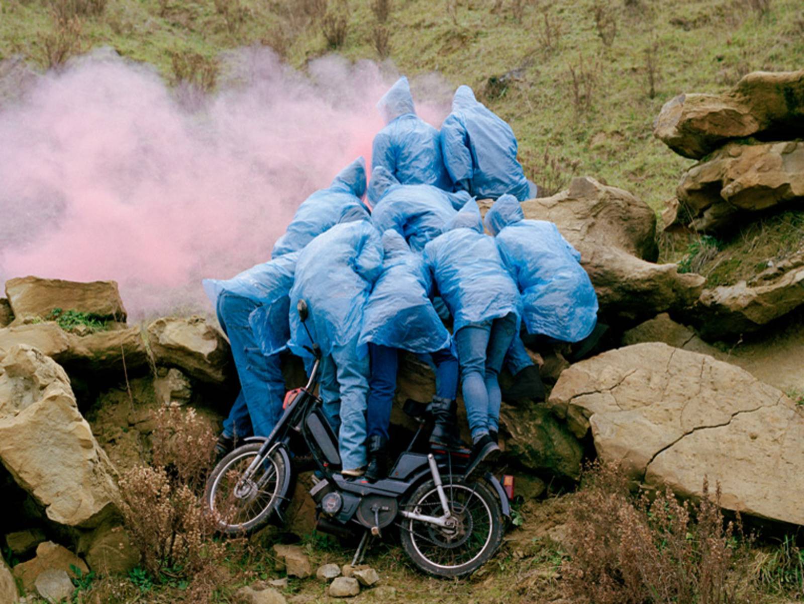 Gruppe aus 9 Menschen mit Regencapes und Fahrrad an einer Felswand