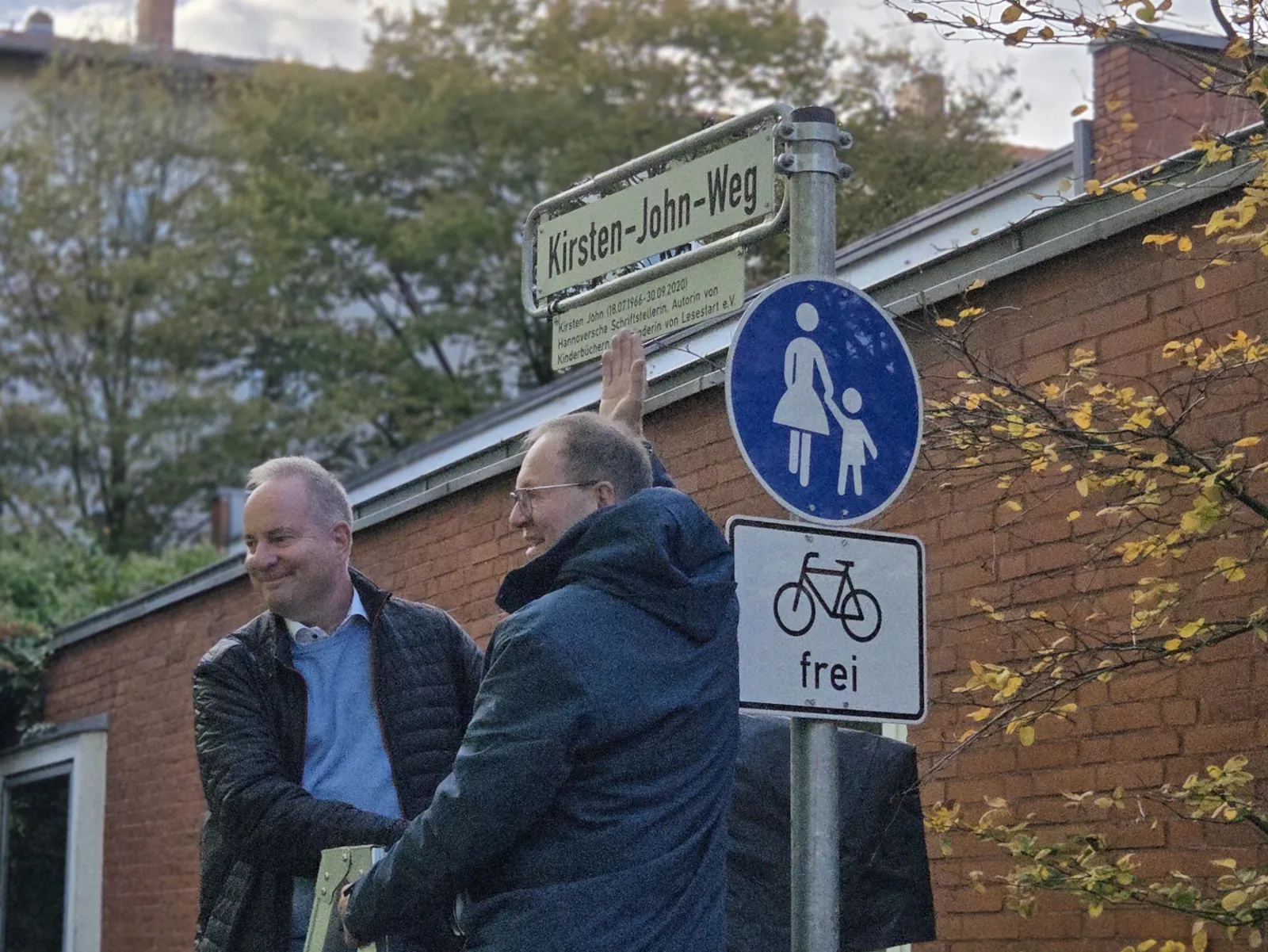 Bezirksb&uuml;rgermeister Herr Meese sowie der Witwer der verstorbenen Namensgeberin, Herr John, enth&uuml;llen das Stra&szlig;enschild Kirsten-John-Weg.
