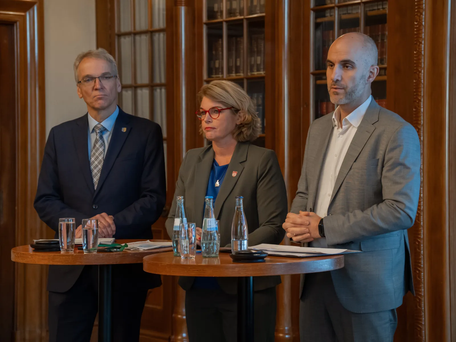 Drei Personen stehen an Stehtischen, vor ihnen stehen Wassergläser.