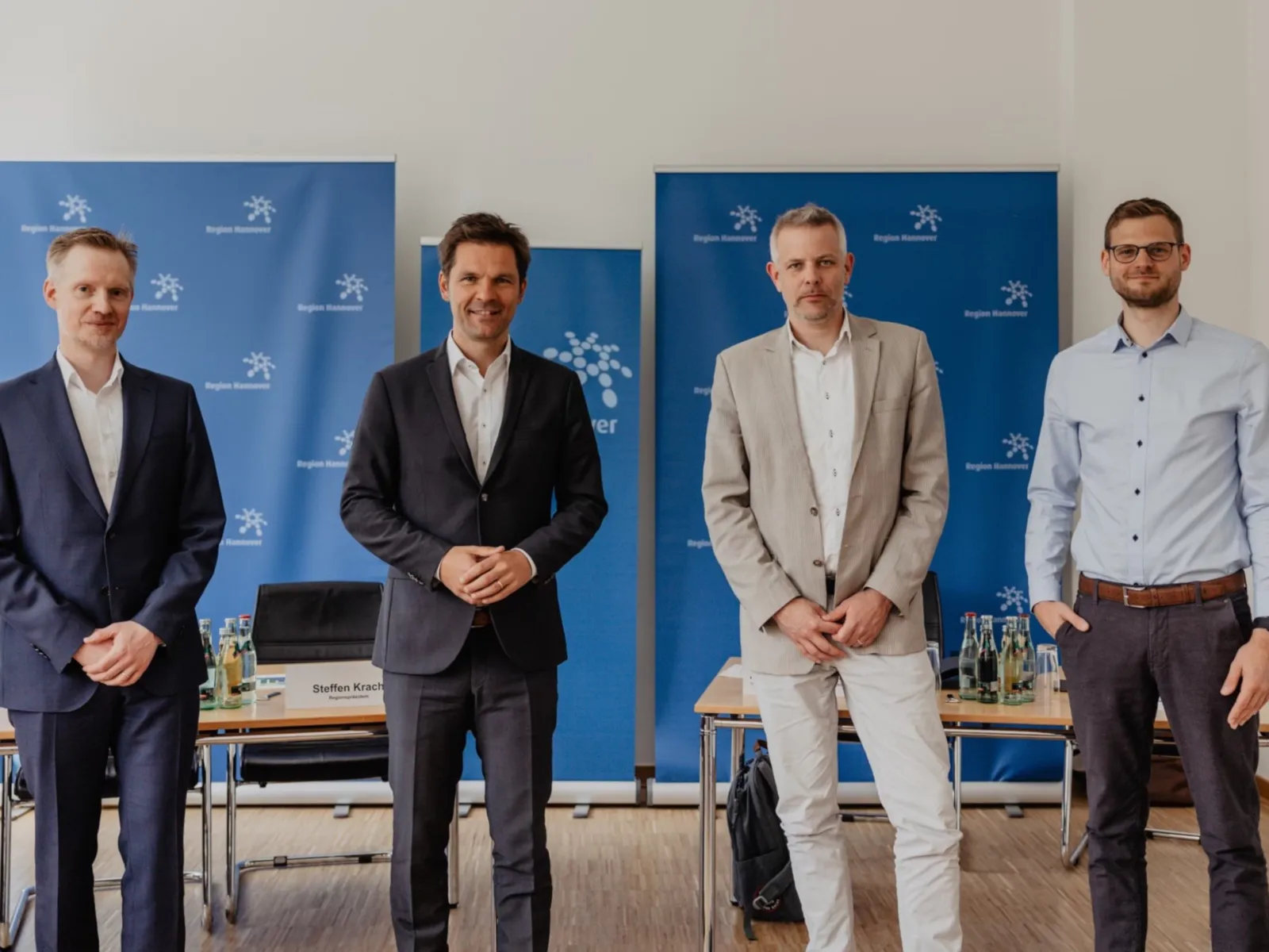 Vier Herren stehen nebeneinander. Im Hintergrund befinden sich Tische und Aufsteller.