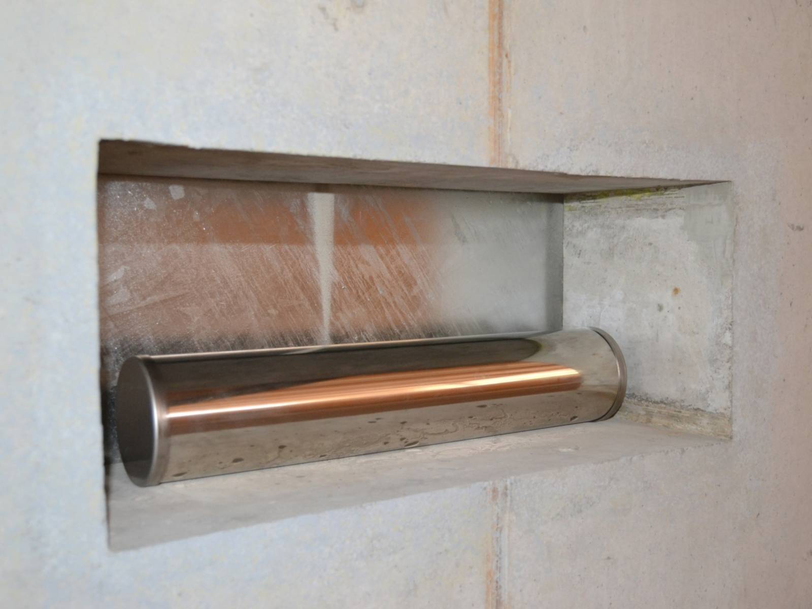 Eine kupferfarbene Metalröhre liegt in einer rechteckigen Maueröffnung.