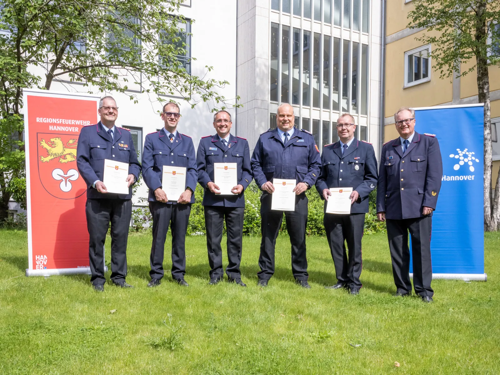 Sechs Herren in Uniform in einem begrünten Innenhof
