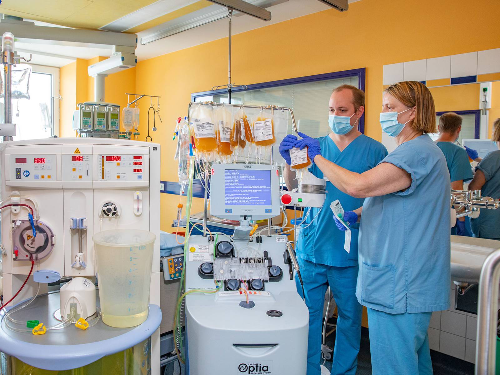 Ein Mann und eine Frau in blauen Kitteln mit Nasen-Mundschutz-Masken in einem medizinischen Labor.