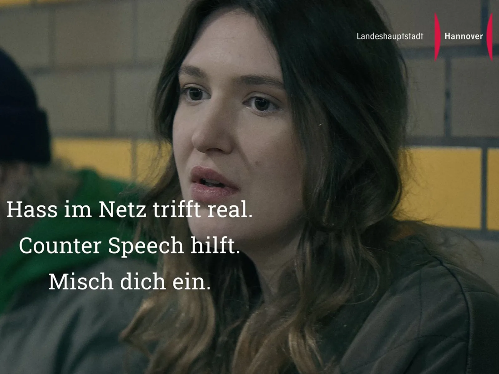 Szene aus einem Video. Man sieht eine eingeschüchterte Frau. Darüber ein Schriftzug.