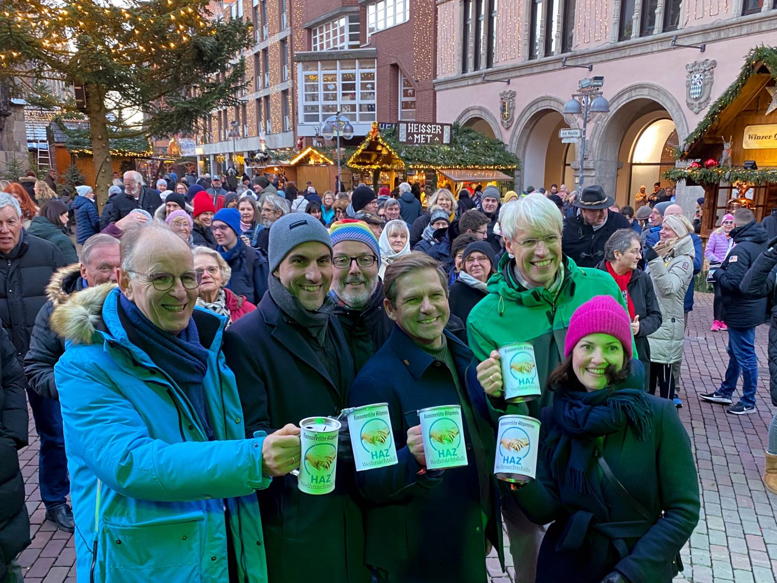 Oberbürgermeister Belit Onayund Stadtsuperintendent Rainer Müller-Brandes mit weiteren Gästen bei der Eröffnung des Weihnachtsmarktes. Sie halten Spendendosen in die Kamera.