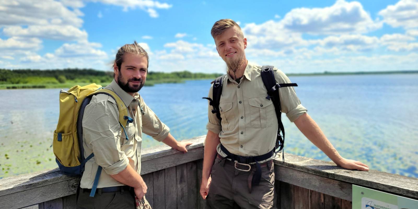 Zwei Männer tragen grüne Kleidung mit dem Logo des Naturparks Steinhuder Meer und stehen auf einem Aussichtsturm.