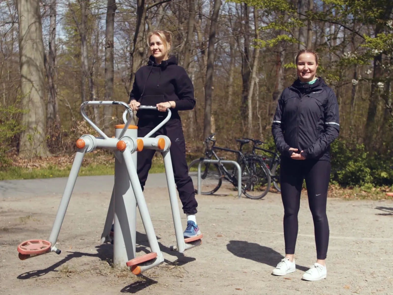 Zwei Frauen an einem Fitnessgerät unter freiem Himmel.