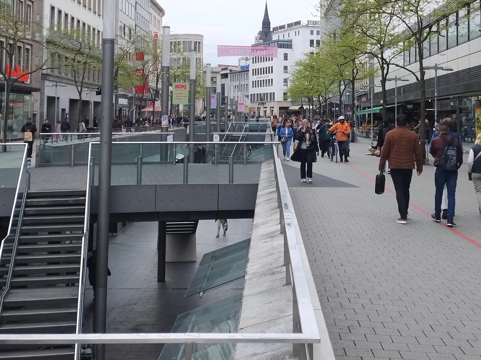 Eine Geschäftsstraße mit Menschen, in der Mitte der Blick in eine Ebene darunter.