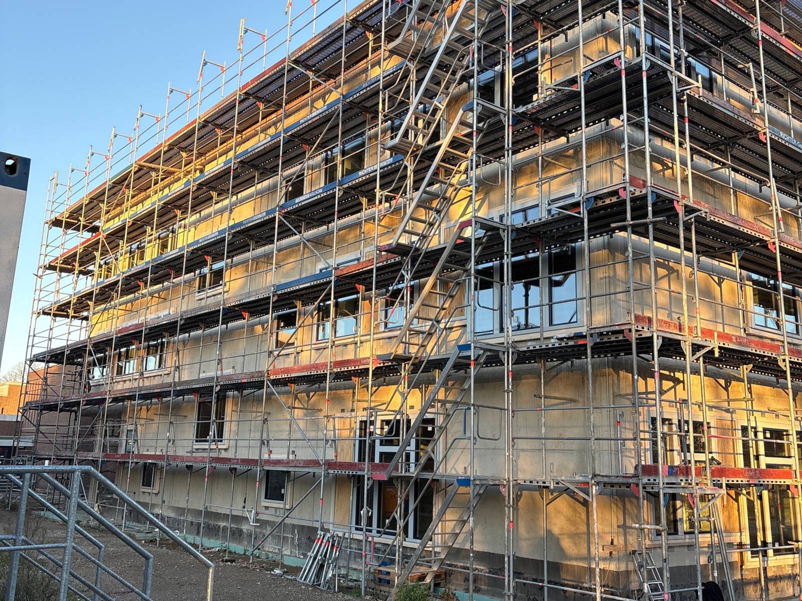 Ein Baugerüst um einen viergeschossigen Rohbau in Bronzefarbe.