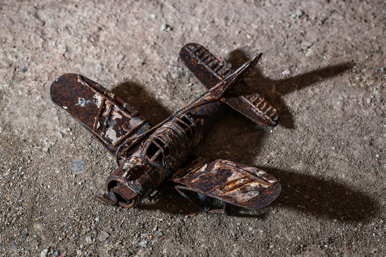 Zu sehen ist eine Fotografie von Stefan Nieland: Ein verrosteter Spielzeugflieger auf dem Boden liegend.