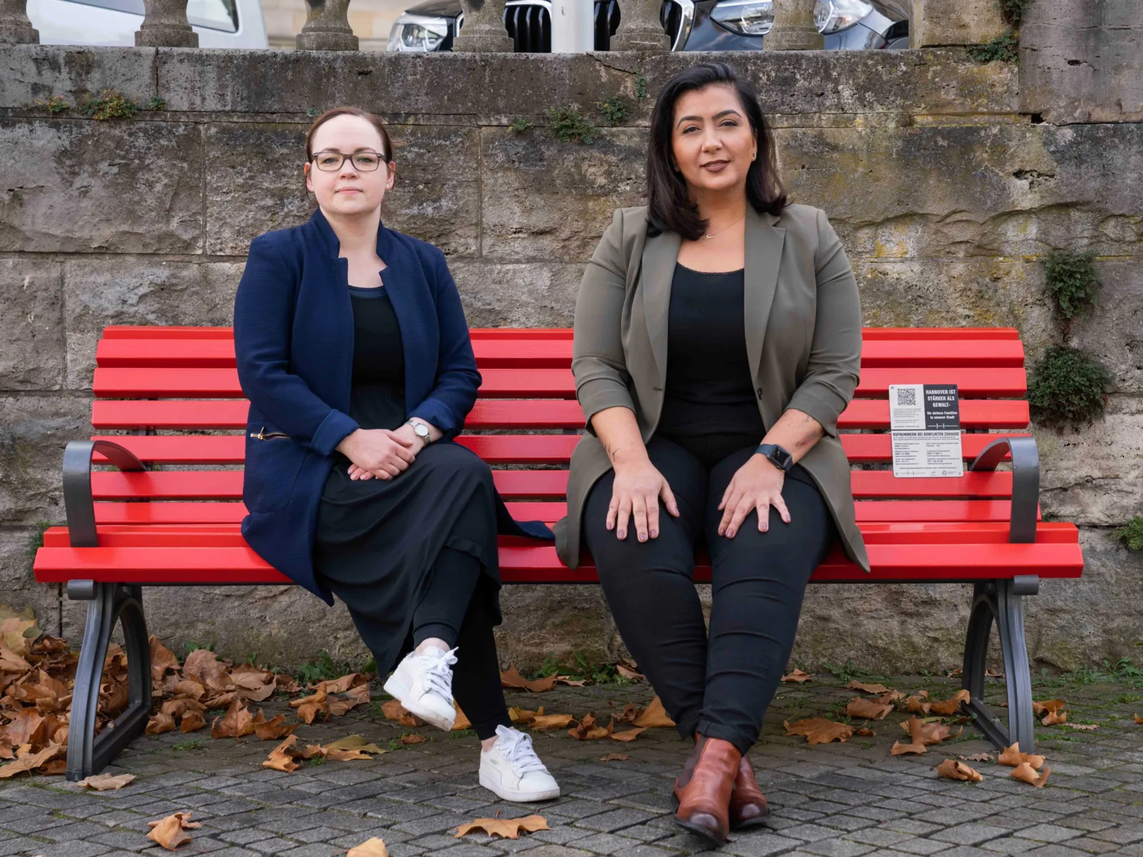 Zwei Personen sitzen auf einer roten Bank.