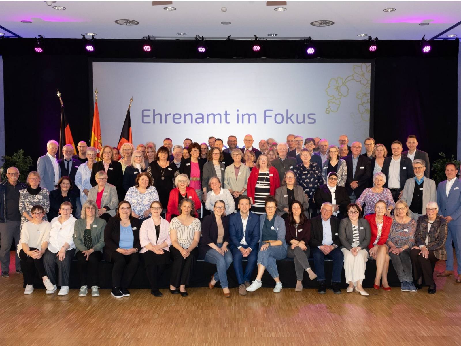 Ein Gruppenfoto mit den Geehrten Personen im Rahmen der Veranstaltung. Auf der Leinwand im Hintergrund steht "Ehrenamt im Fokus".