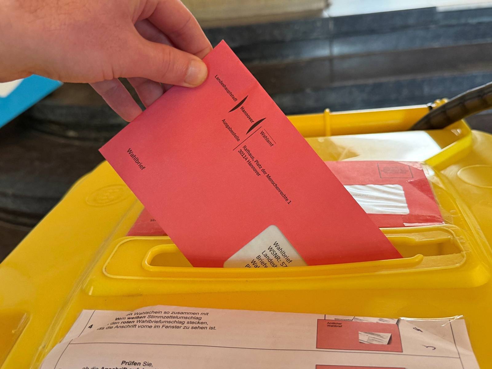 Eine Hand, die einen Brief in eine Wahlurne wirft.