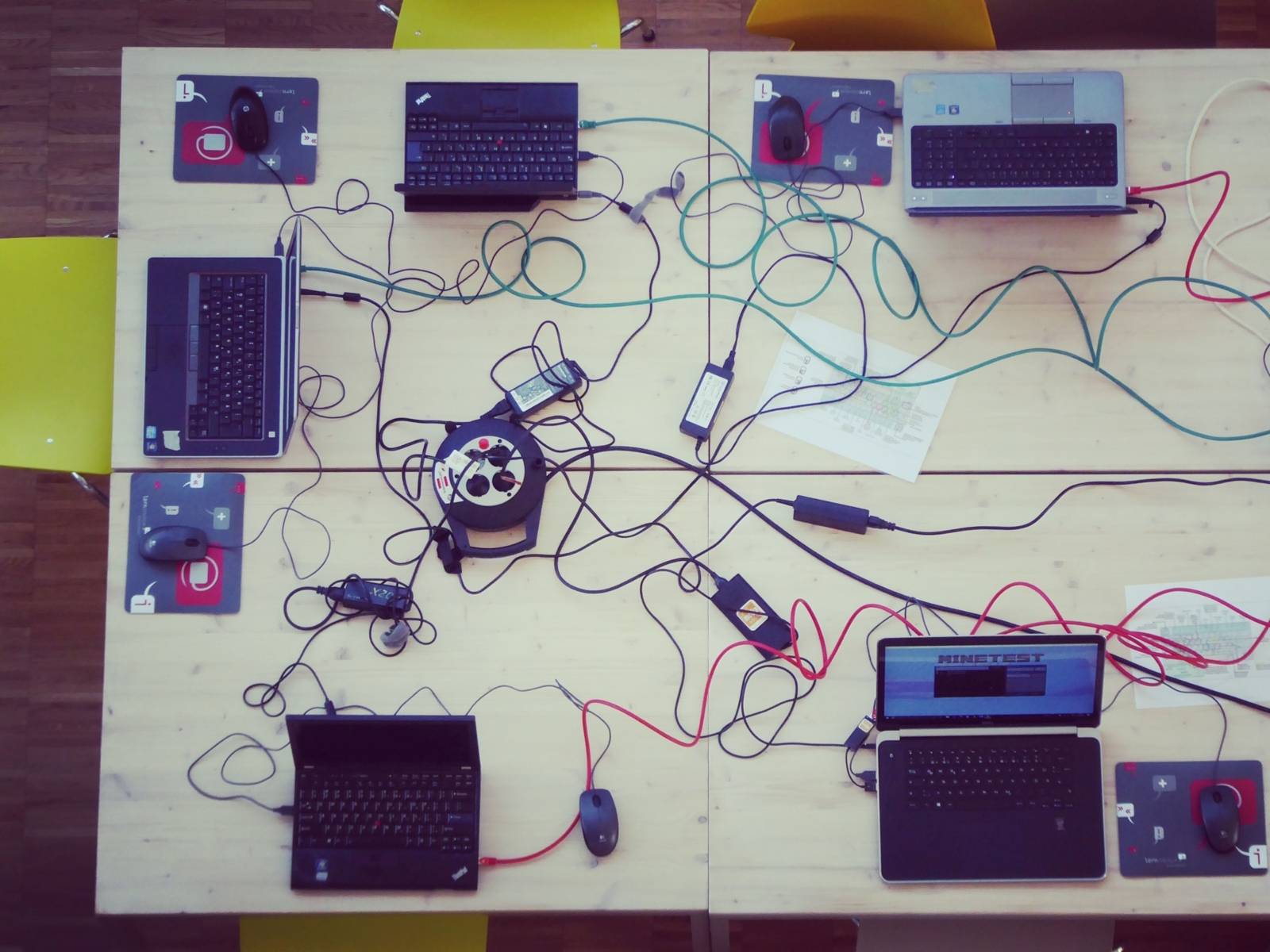 Ein großer Tisch, auf dem einige Laptops stehen, umringt von Kabelgewirr.