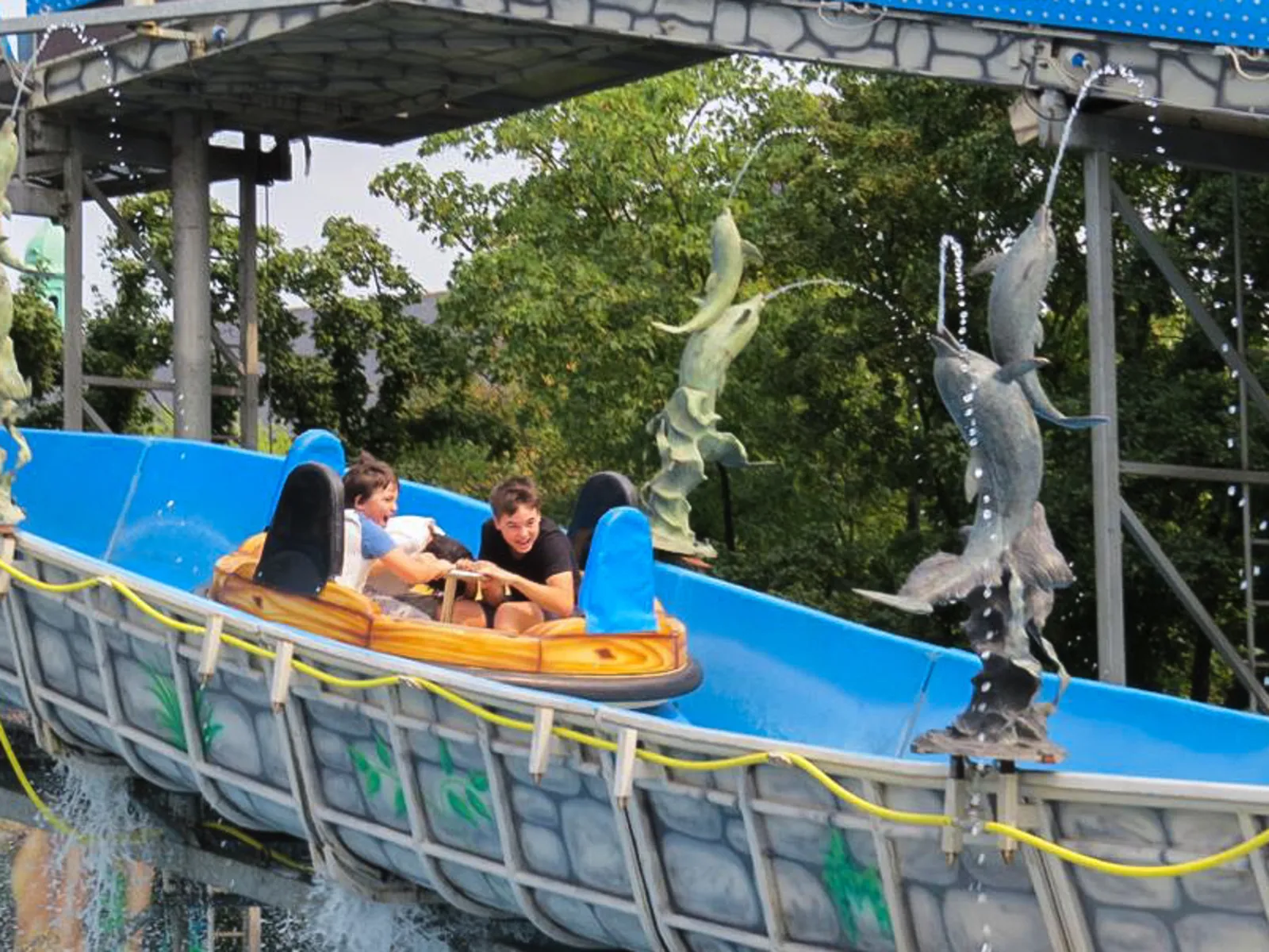 Ein Fahrgeschäft auf einem Volksfest. Darin sitzen drei Kinder, die gerade einen Wasserkanal hinabsausen.