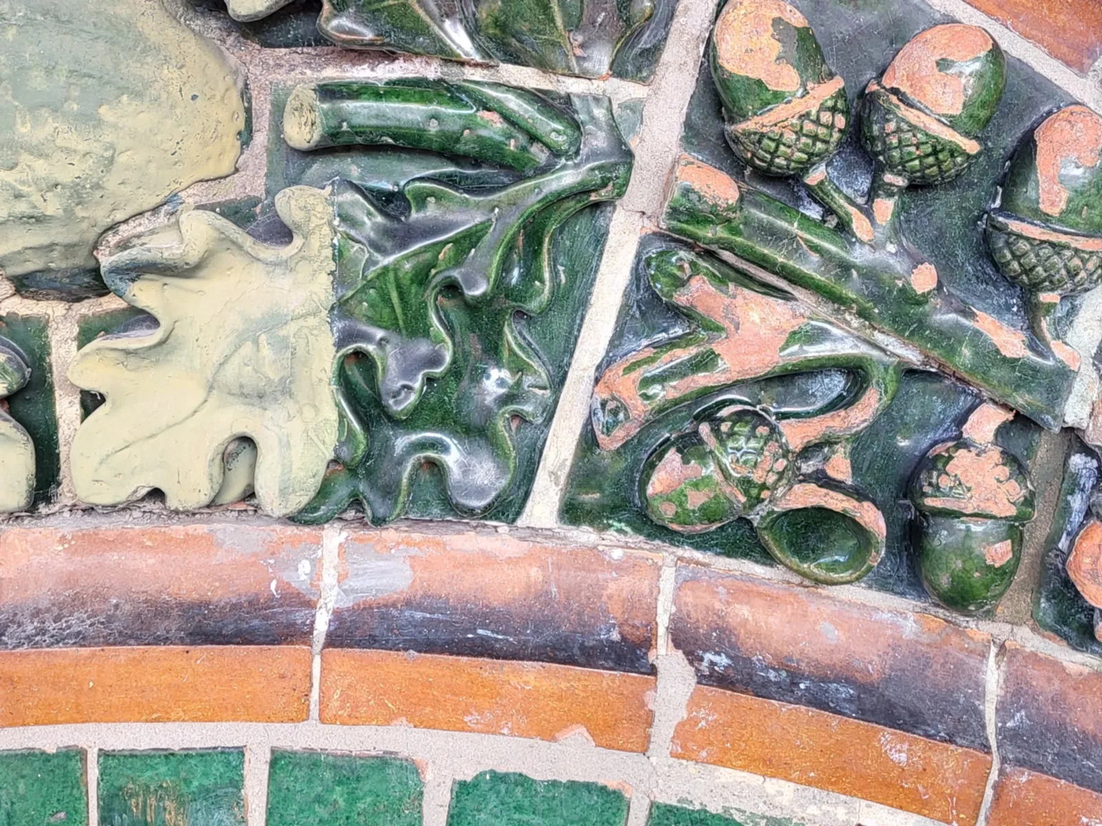 Detail einer Hausfassade  mit grünen und backsteinroten Steinen und grünen Verzierungen in Form von Blättern und Eicheln