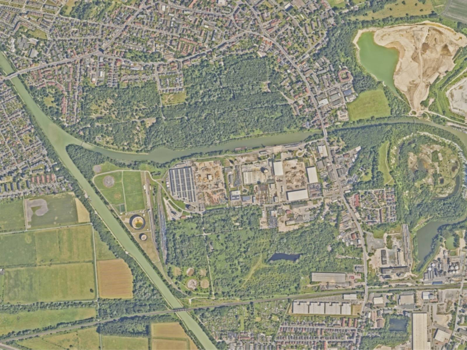 Blick von oben auf eine Landschaft mit viel Grün, Bäumen, Häuseransammlungen, Straßen und einem Kanal.