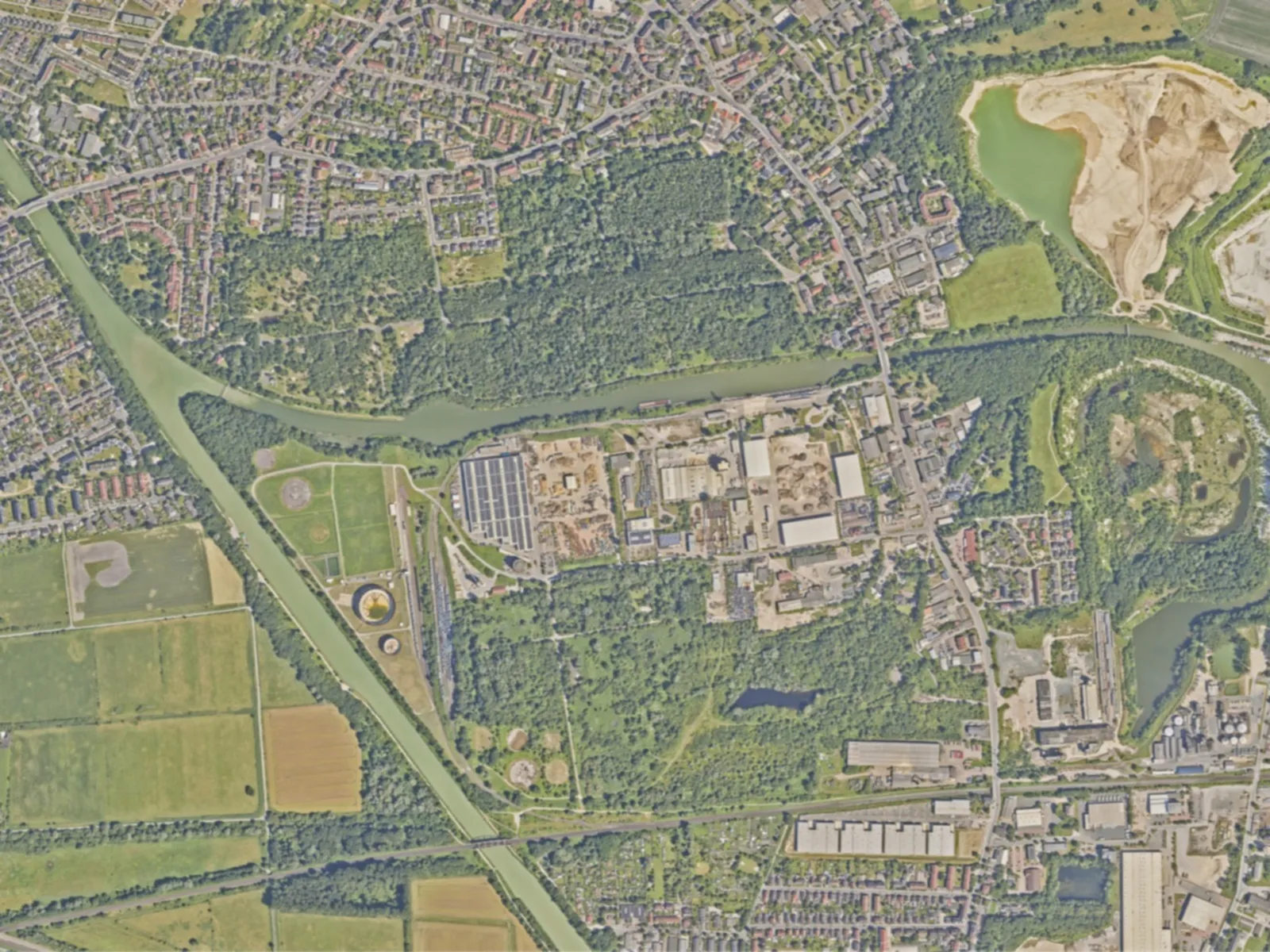 Blick von oben auf eine Landschaft mit viel Grün, Bäumen, Häuseransammlungen, Straßen und einem Kanal.