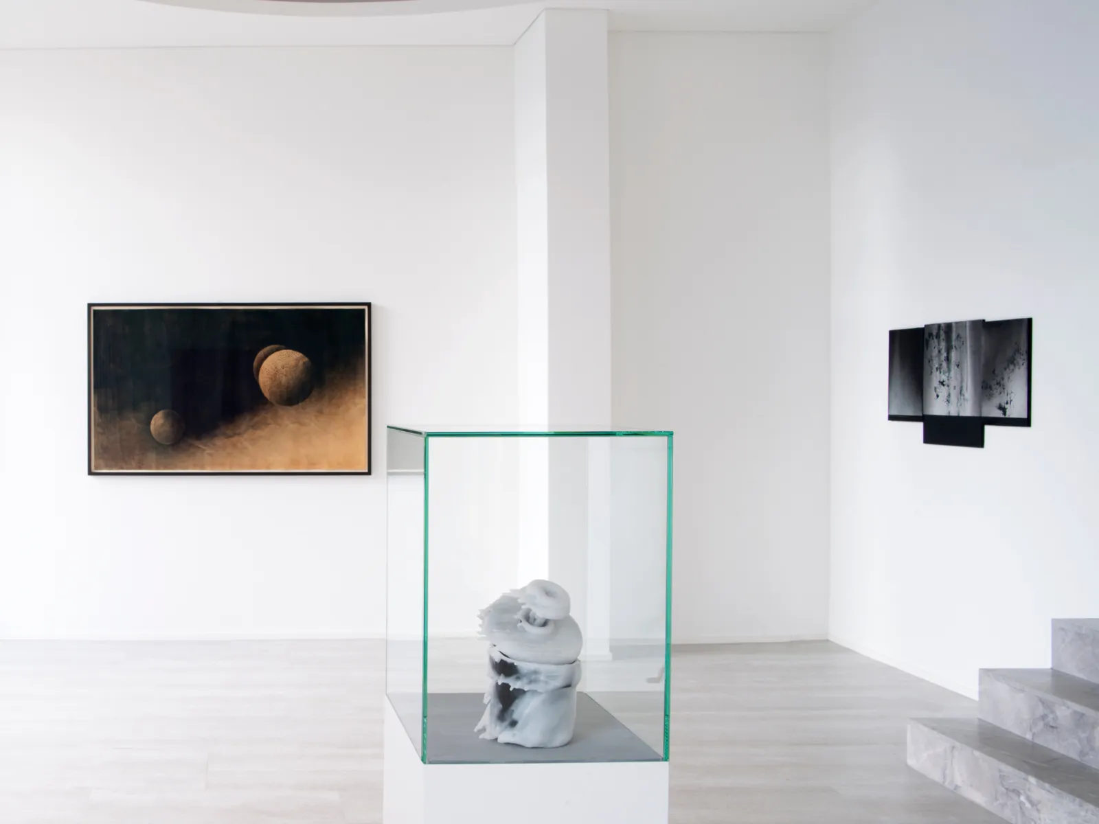 Moderne Galerie mit Skulptur in Glaskasten und zwei abstrakten Wandbildern auf weißem Hintergrund.