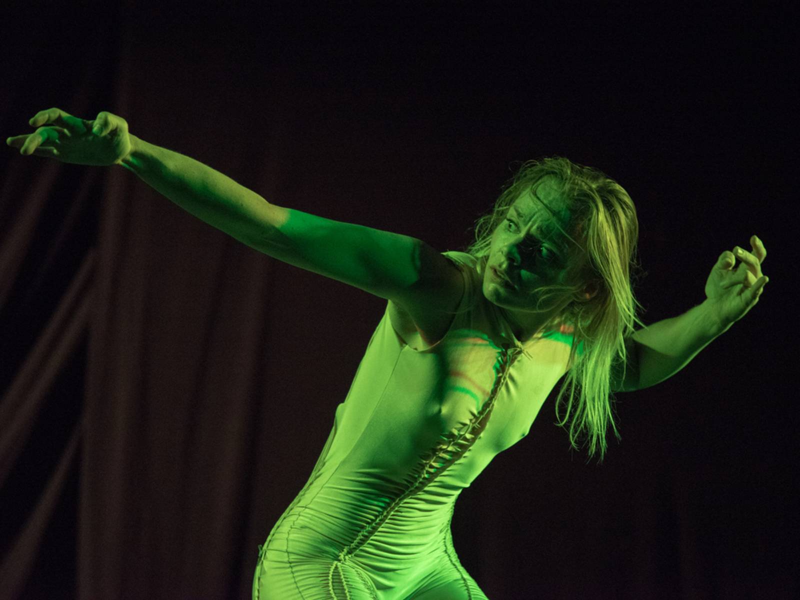Eine Frau tanzt, dabei ist sie in grünes Licht getaucht.