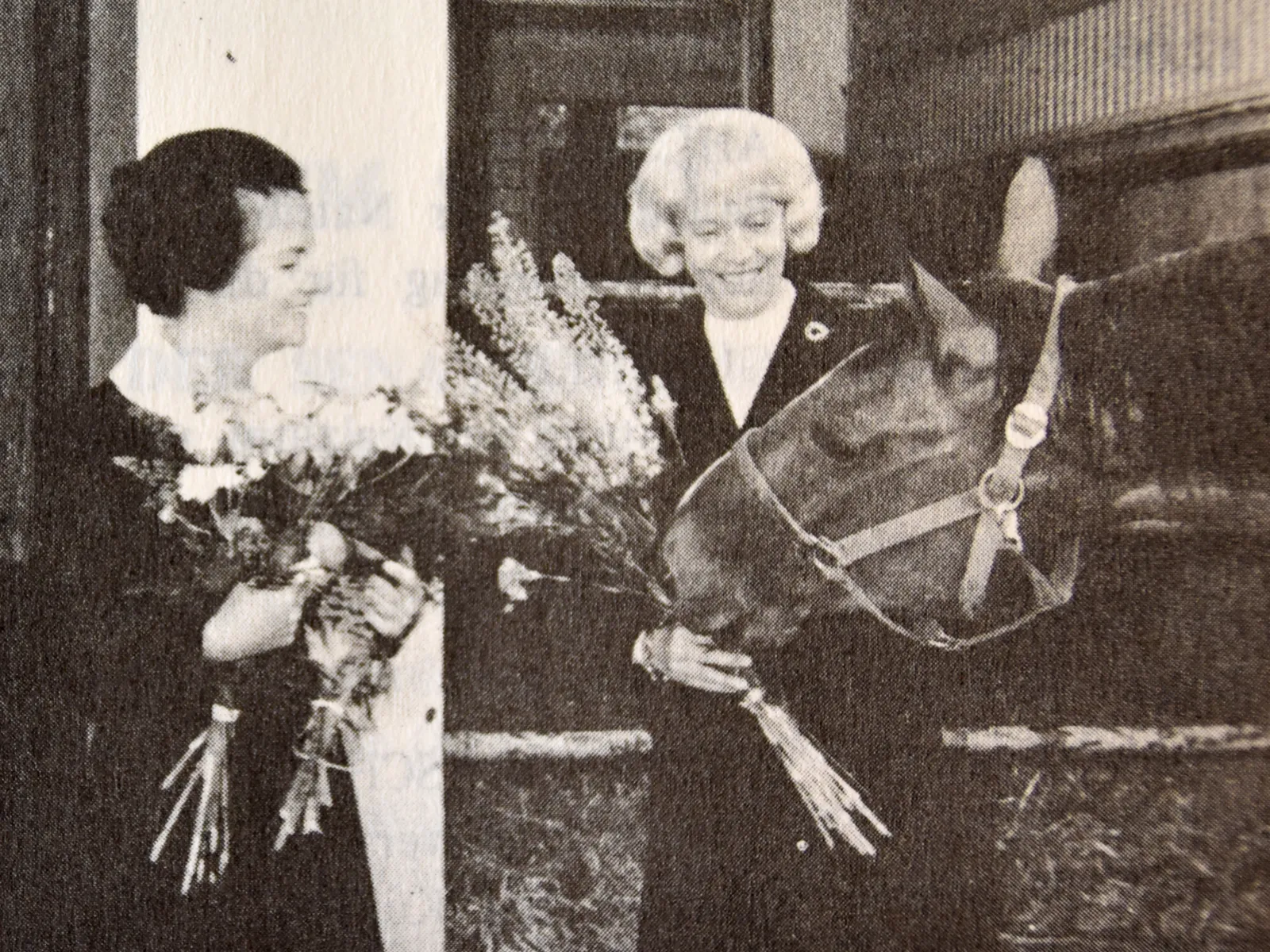 Zwei Frauen mit Blumensträußen in den Händen und ein Pferd (schwarz-weiß-Bild).