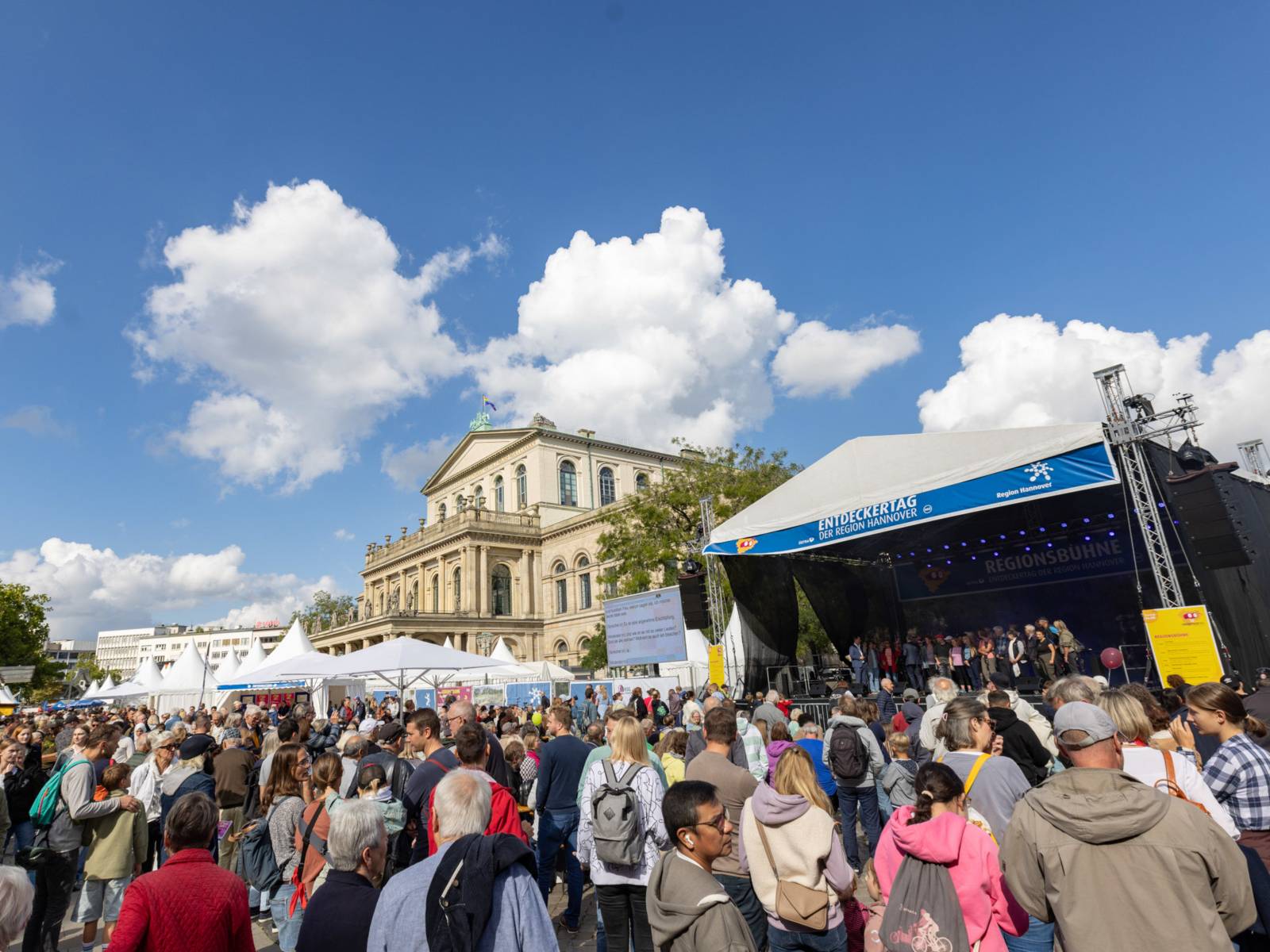 Menschen vor einer Bühne, im Hintergrund ist das Opernhaus Hannover zu sehen.