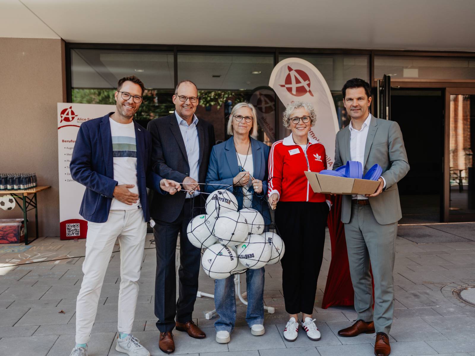 Fünf Menschen mit Fußbällen und Frisbees vor der neuen Turnhalle der Alice Salomon Schule