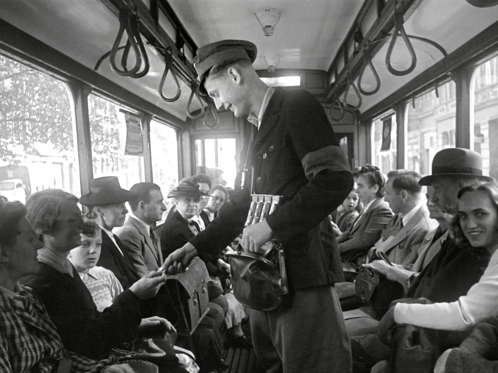 Schwarz-Wei&szlig;-Fotografie: Ein Mann tr&auml;gt eine Dienstm&uuml;tze und verkauft Fahrscheine gegen Bargeld in einer Stra&szlig;enbahn.